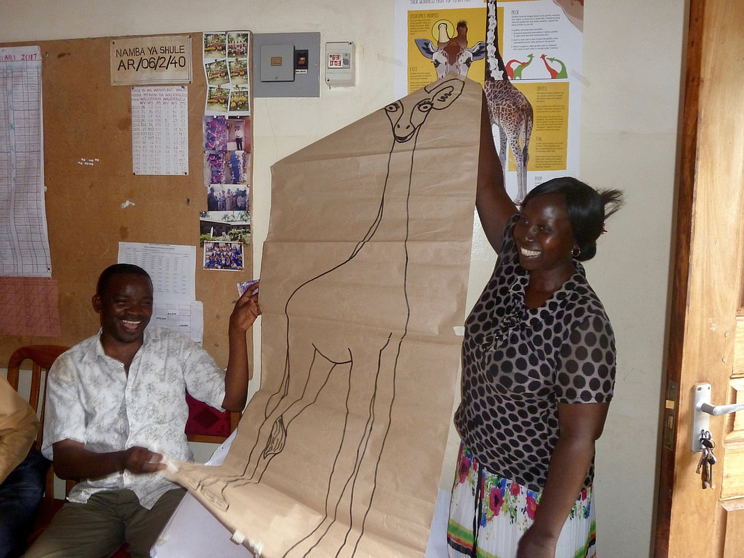 Two people hold up a drawing of a giraffe created with this curriculum.